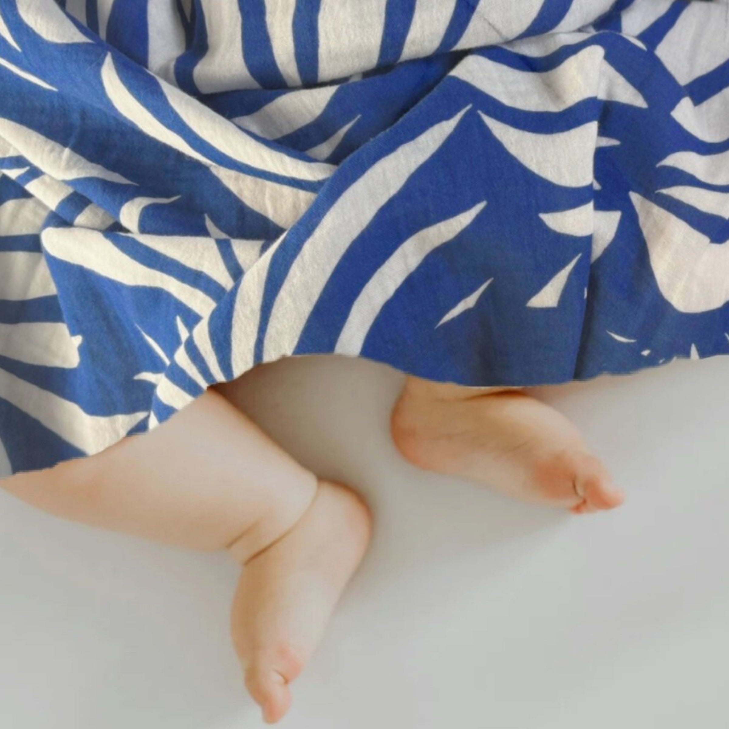 A newborn snuggling in Azul Tropique Small Square muslin nearby, showing comfort and softness in early days.