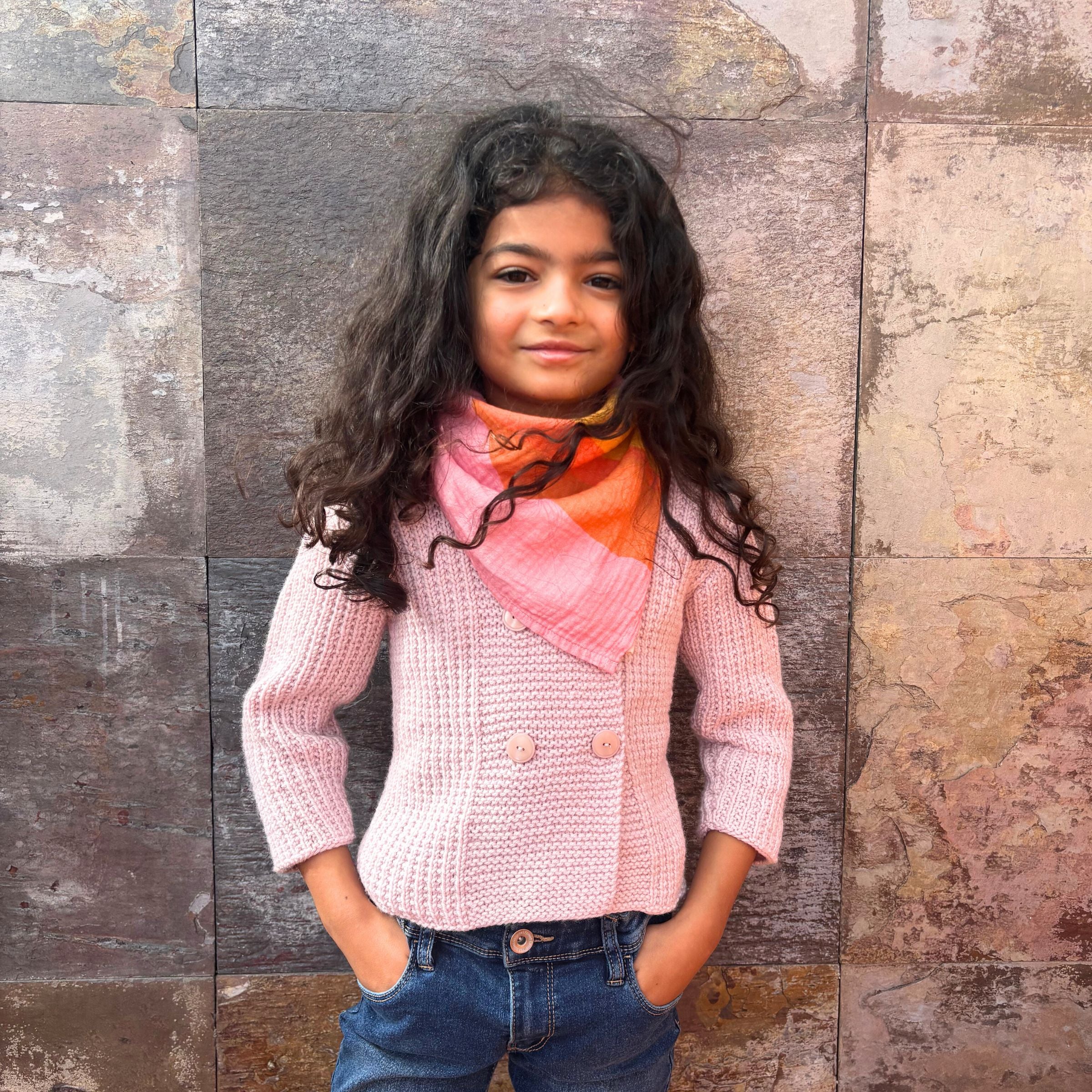 A girl wearing the Indra Small Square muslin as a neck scarf, demonstrating continued use as the child grows.