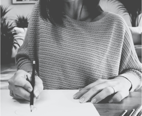 Black and white image of hands writing thoughtfully with a pencil, symbolizing mindfulness and the creative process in design.