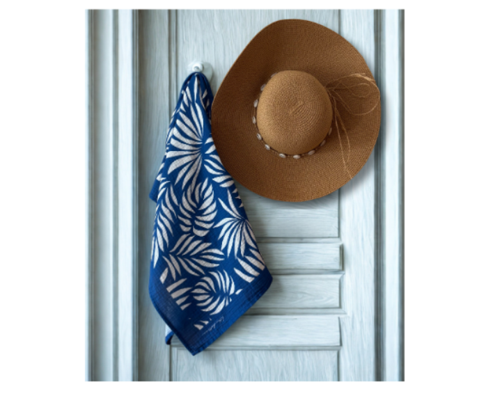 A stylish straw hat and a blue Azul Tropique muslin draped over a white door, embodying intentional design and everyday luxury.
