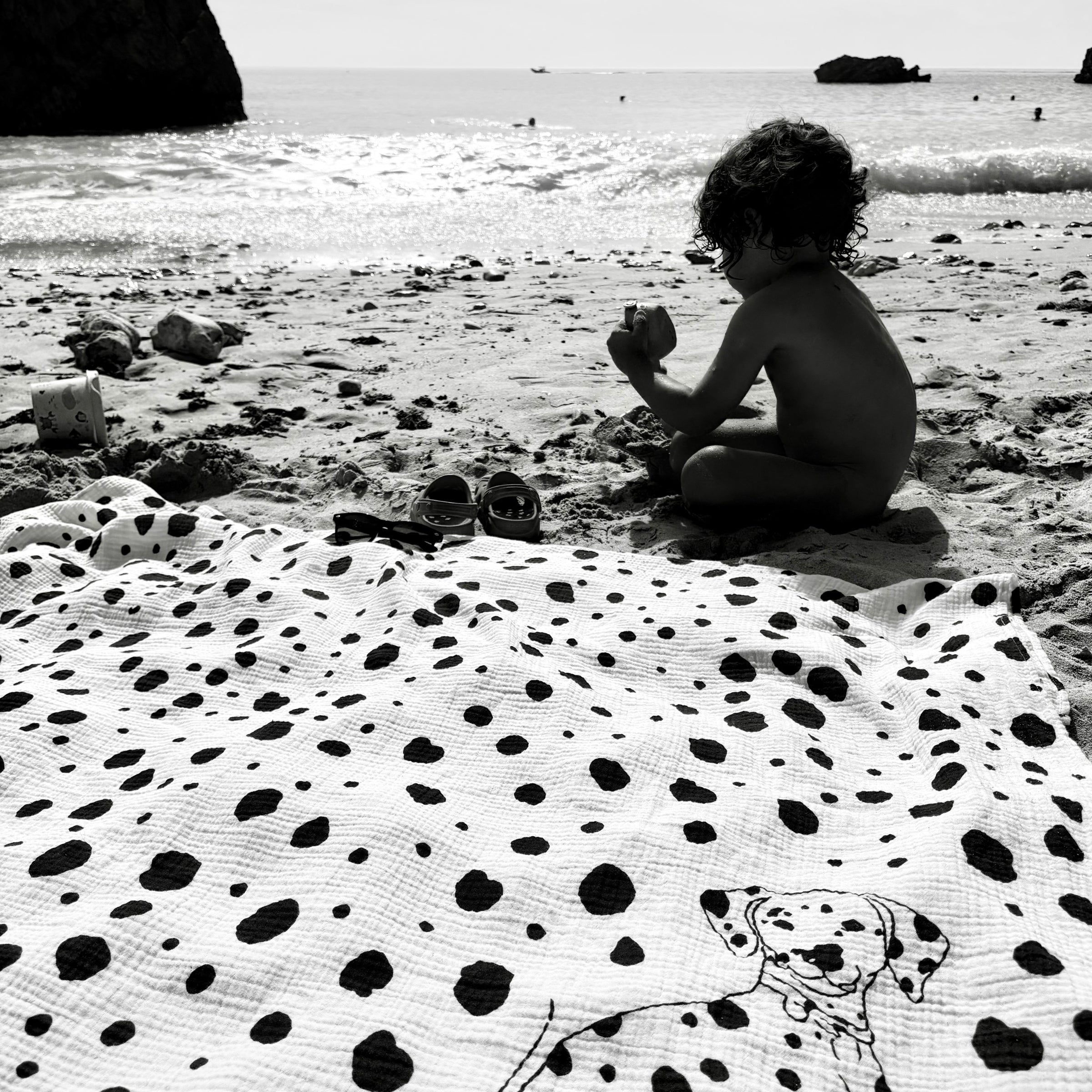 Child playing on a beach with a Dalmatian Allure en Noir Large Square Muslin Blanket