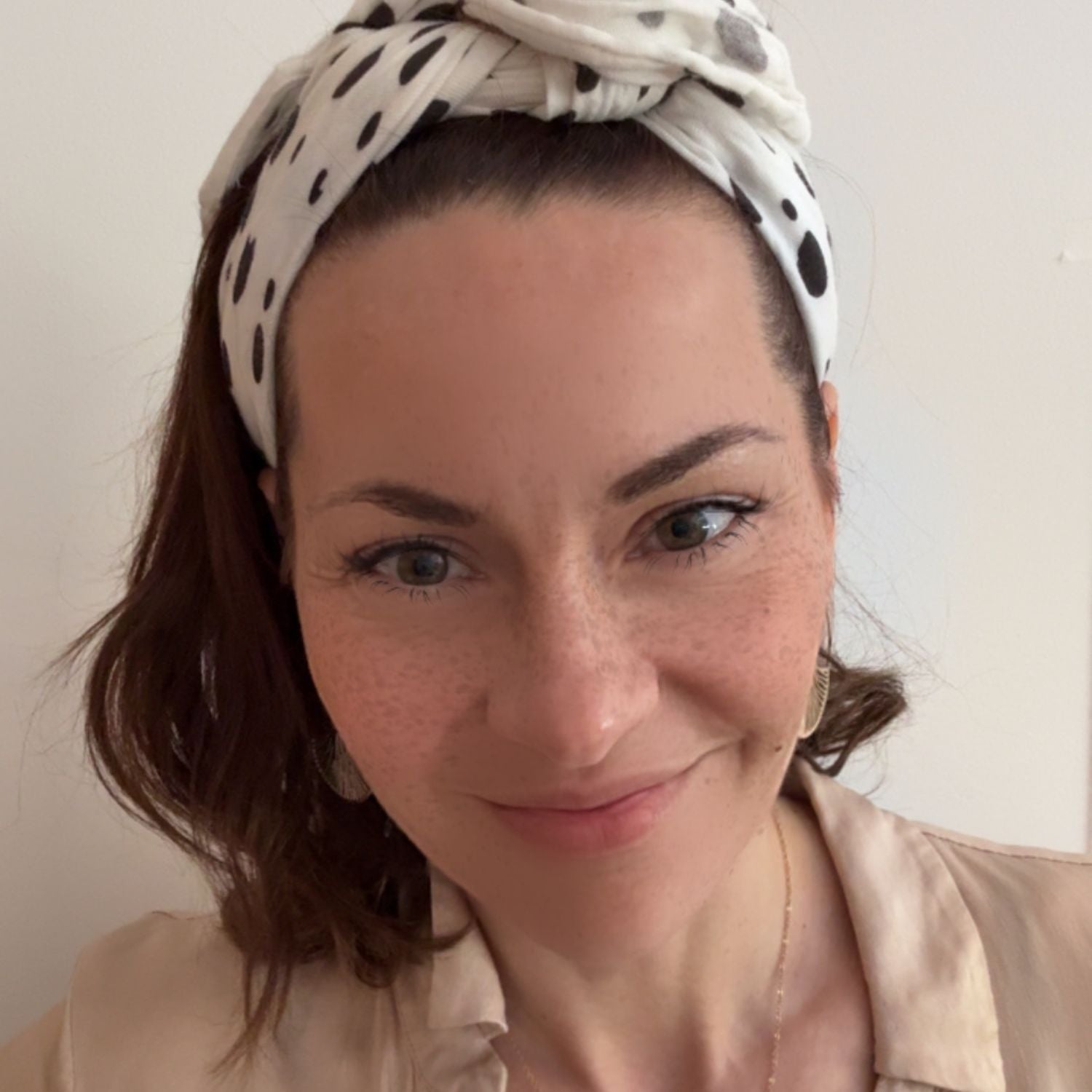 An adult wearing the Small Square Allure en Noir muslin as a headscarf, showing styling beyond the newborn phase.
